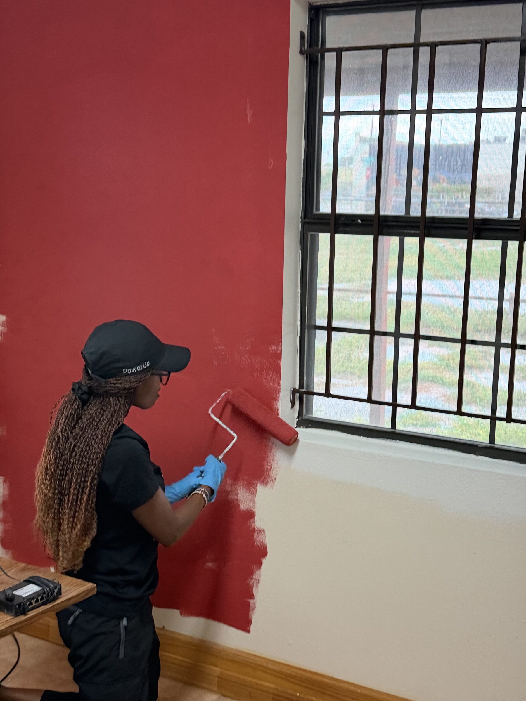 A volunteer rolling red paint beside a barred window