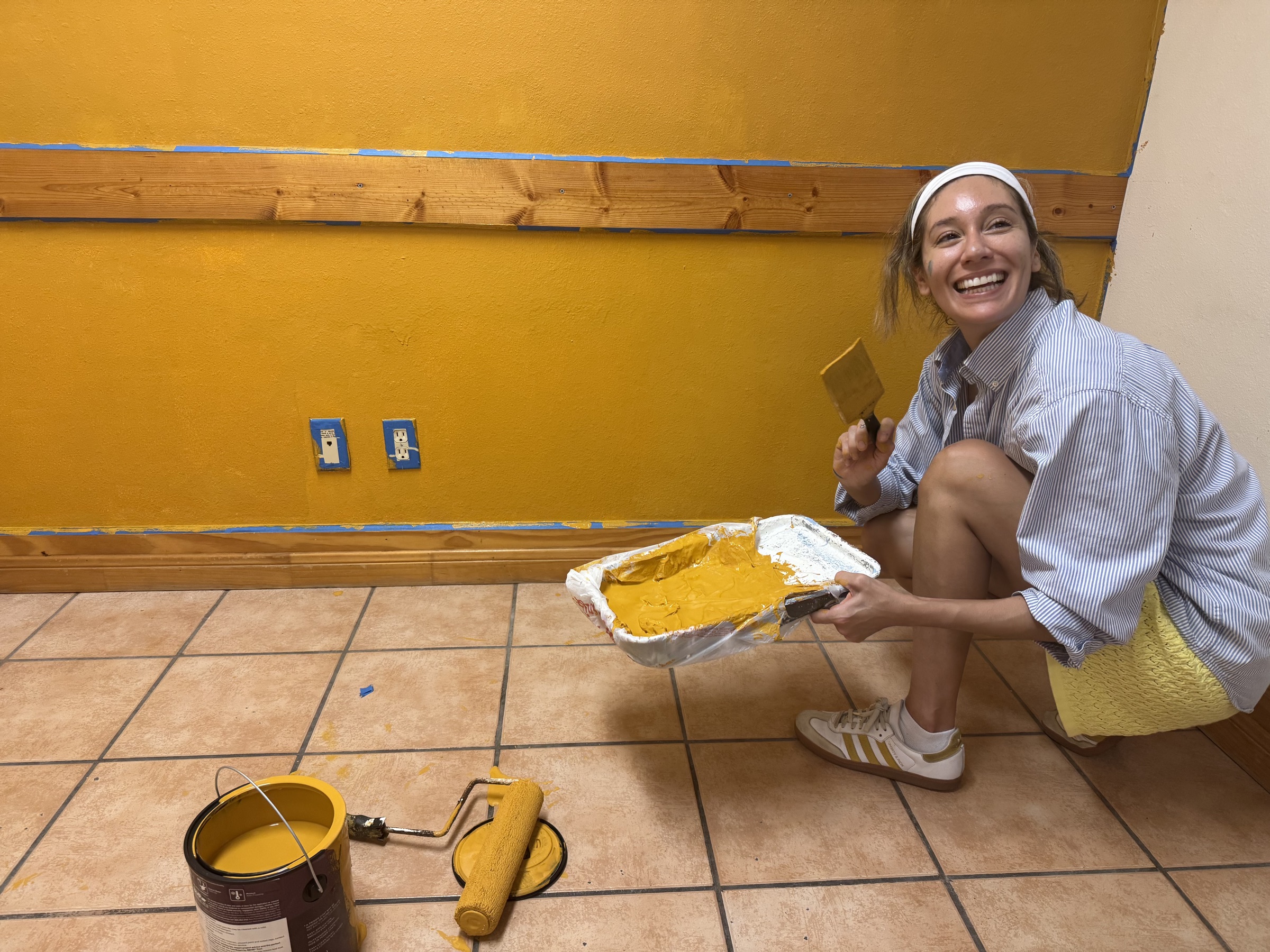 A volunteer crouching to paint a yellow wall