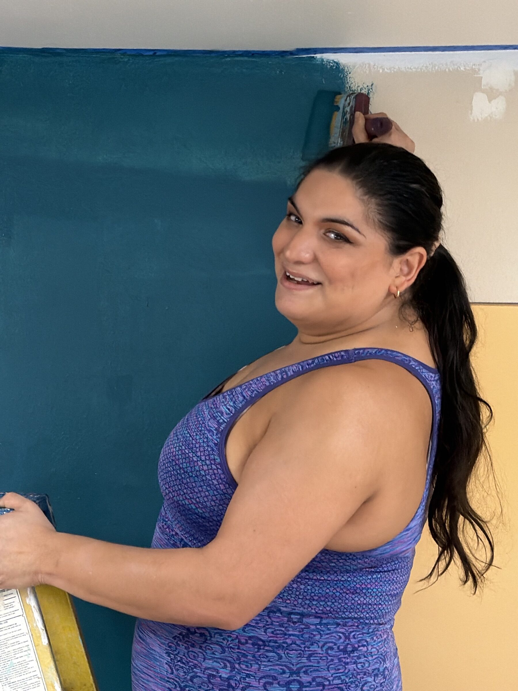 A volunteer on a ladder painting the teal wall