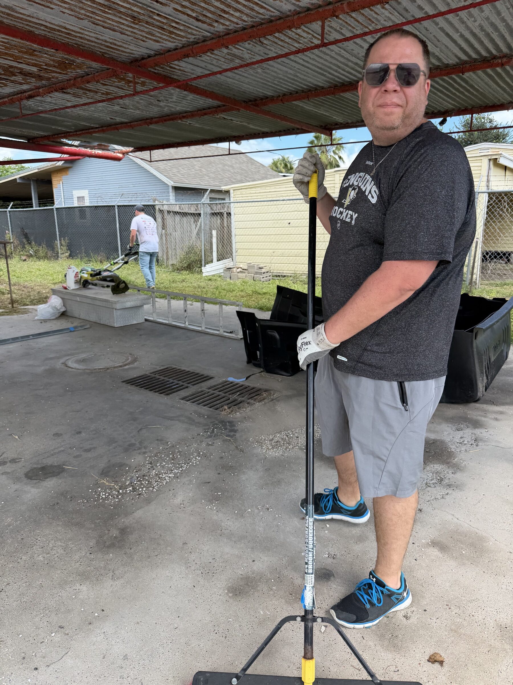A volunteer sweeping the yard under the carport
