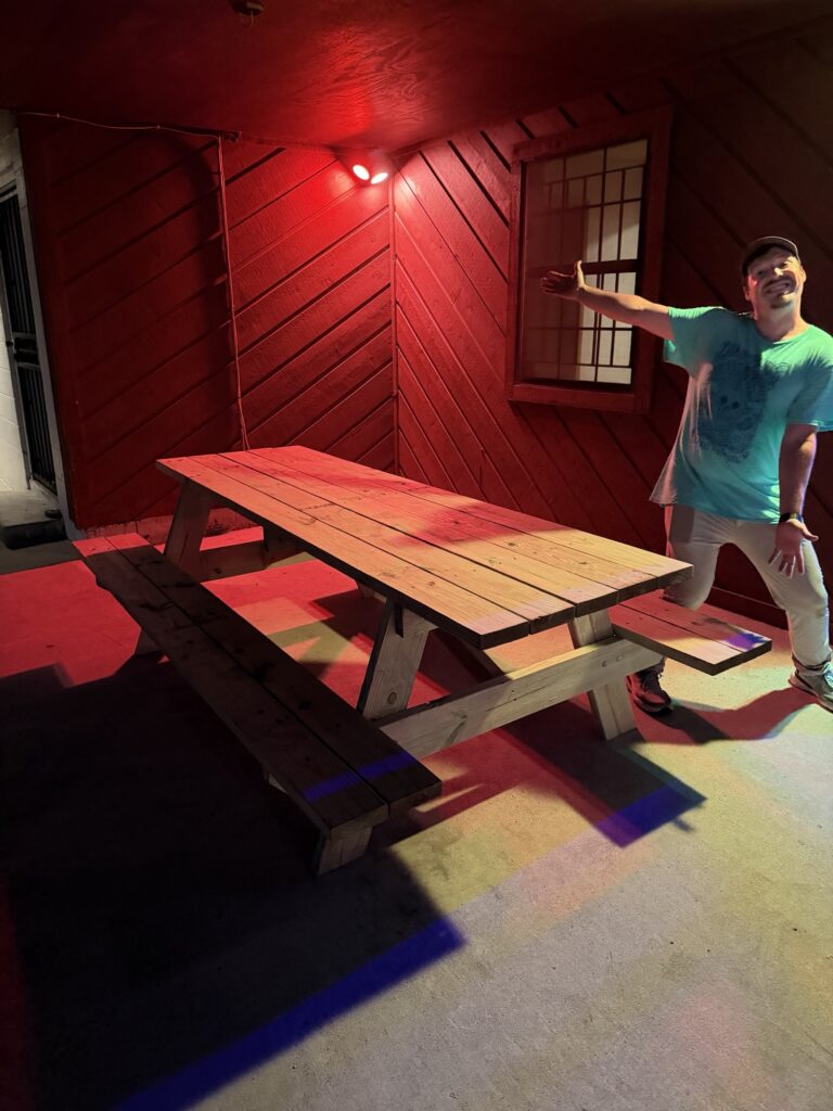 A new handmade wooden picnic table on the Center's patio under red lights