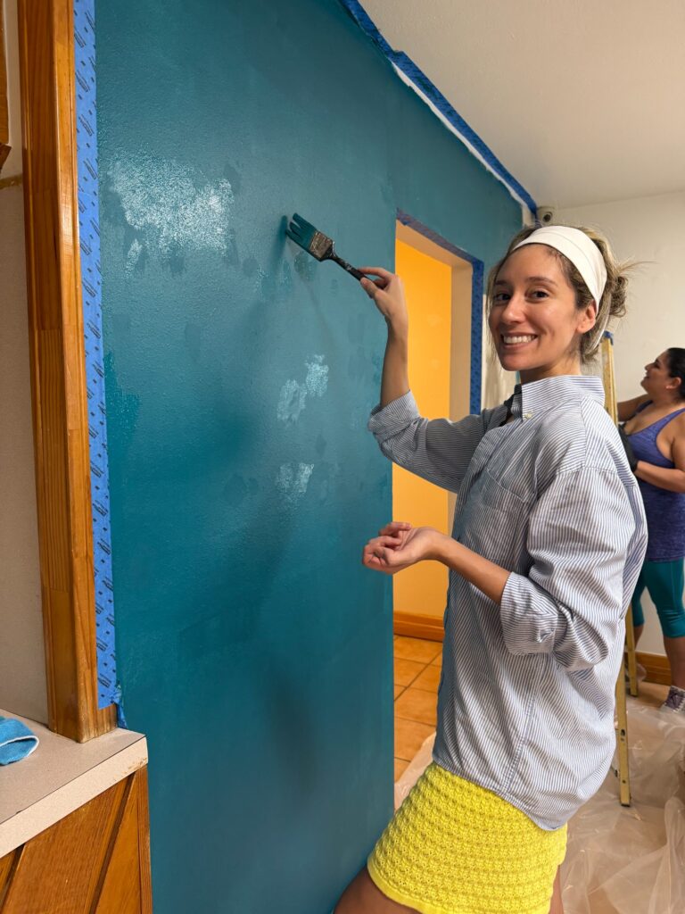 A volunteer smiling while painting the teal wall