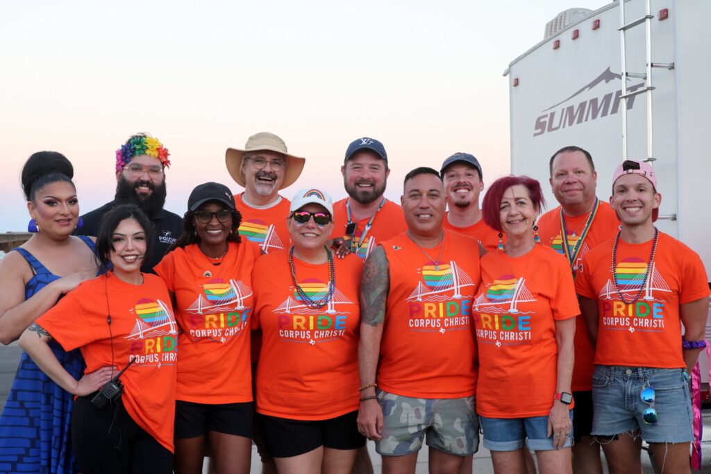 The Pride Corpus Christi board in orange shirts at sunset
