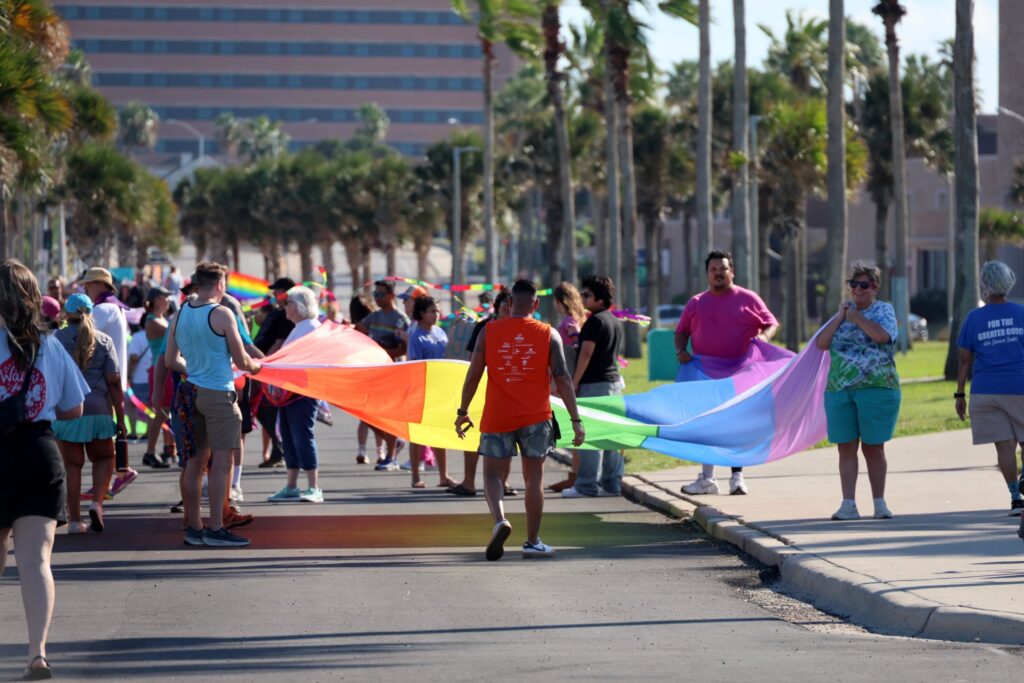 The parade carrying a long rainbow flag down a palm-lined Shoreline Boulevard